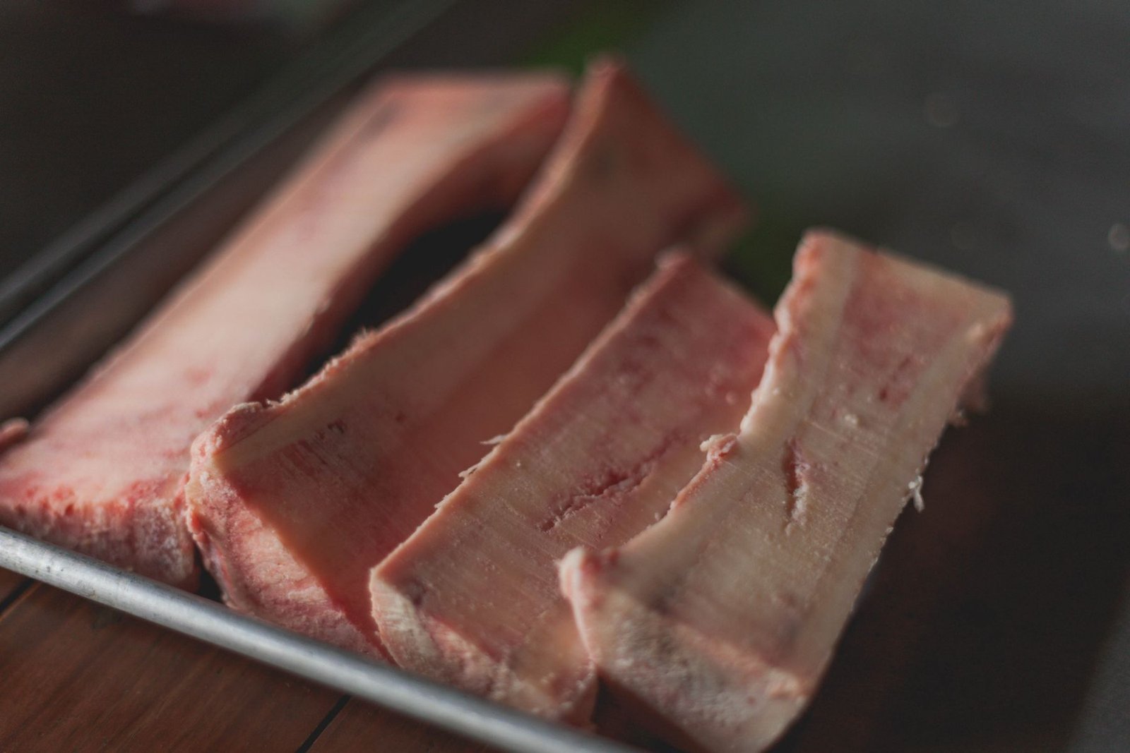 Raw beef marrow bones split lengthwise and lined up on a metal tray.