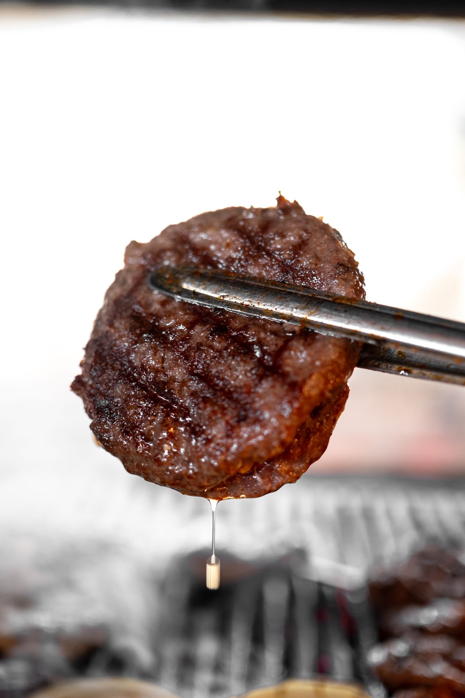 A juicy grilled beef patty held in metal tongs.