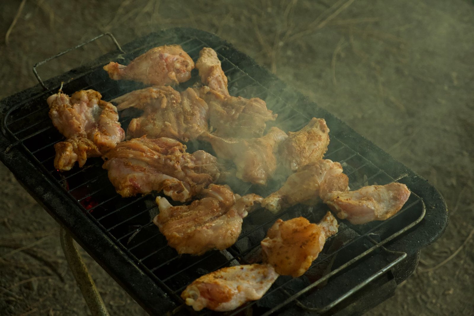 Chicken wings cooking over charcoal with smoke moving across the grate.