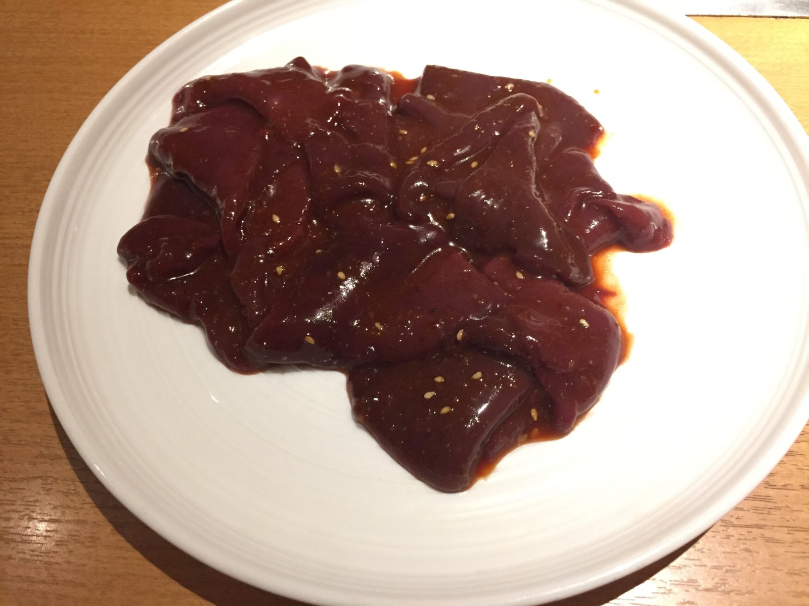 Thin slices of raw beef liver on a plain white plate.