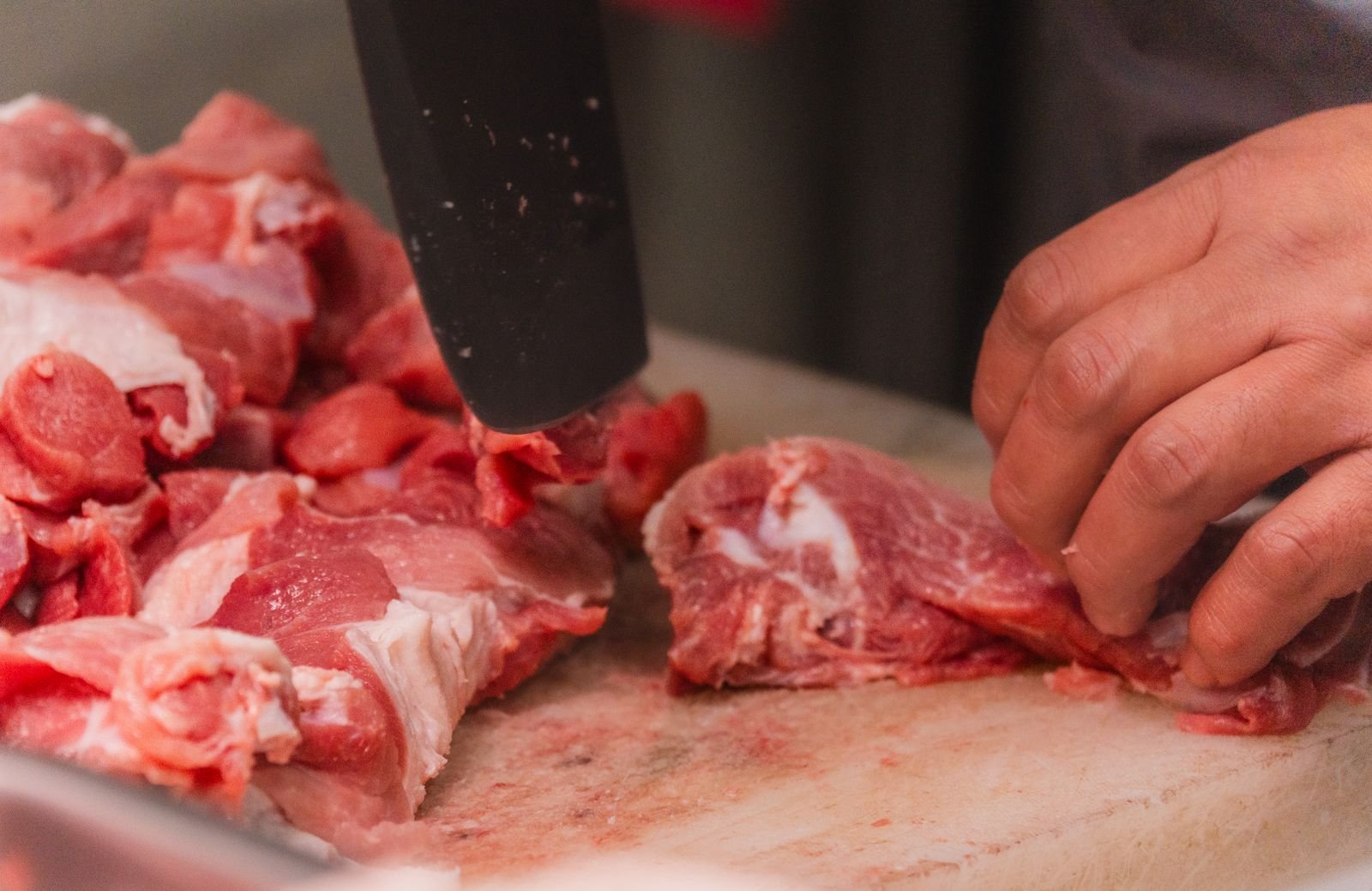 A butcher cutting raw meat into even pieces with a cleaver.