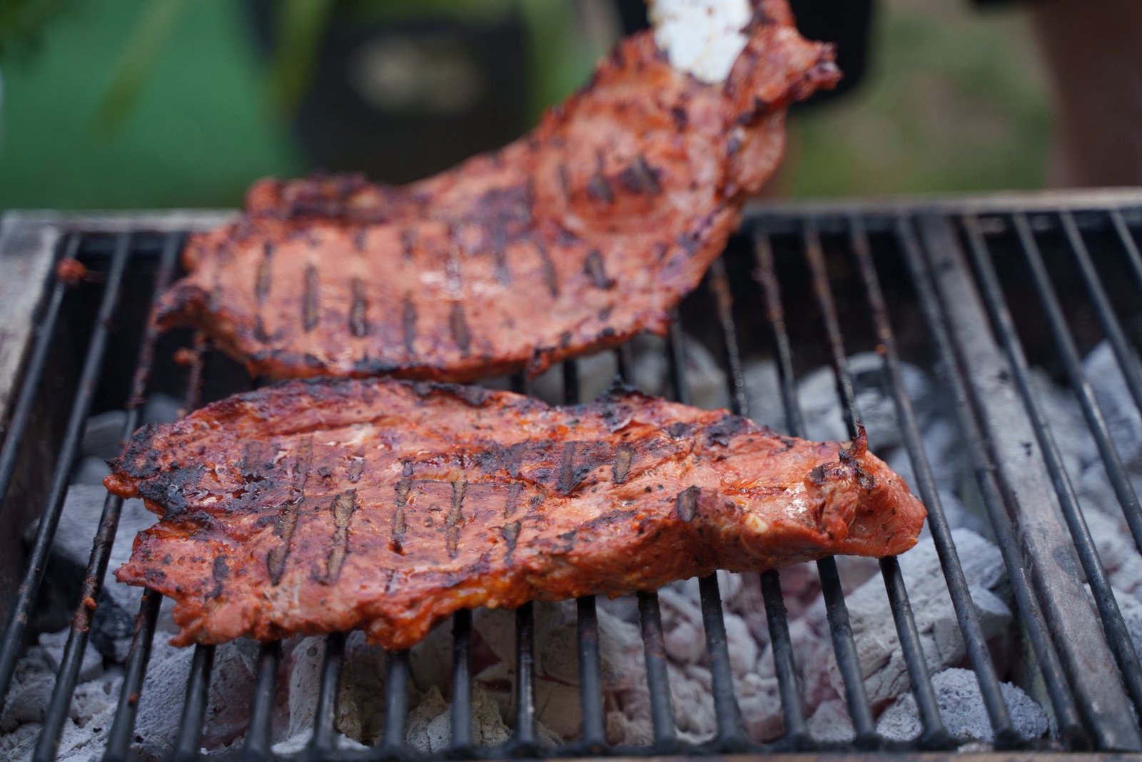Two racks of pork ribs browning directly over a charcoal grill.