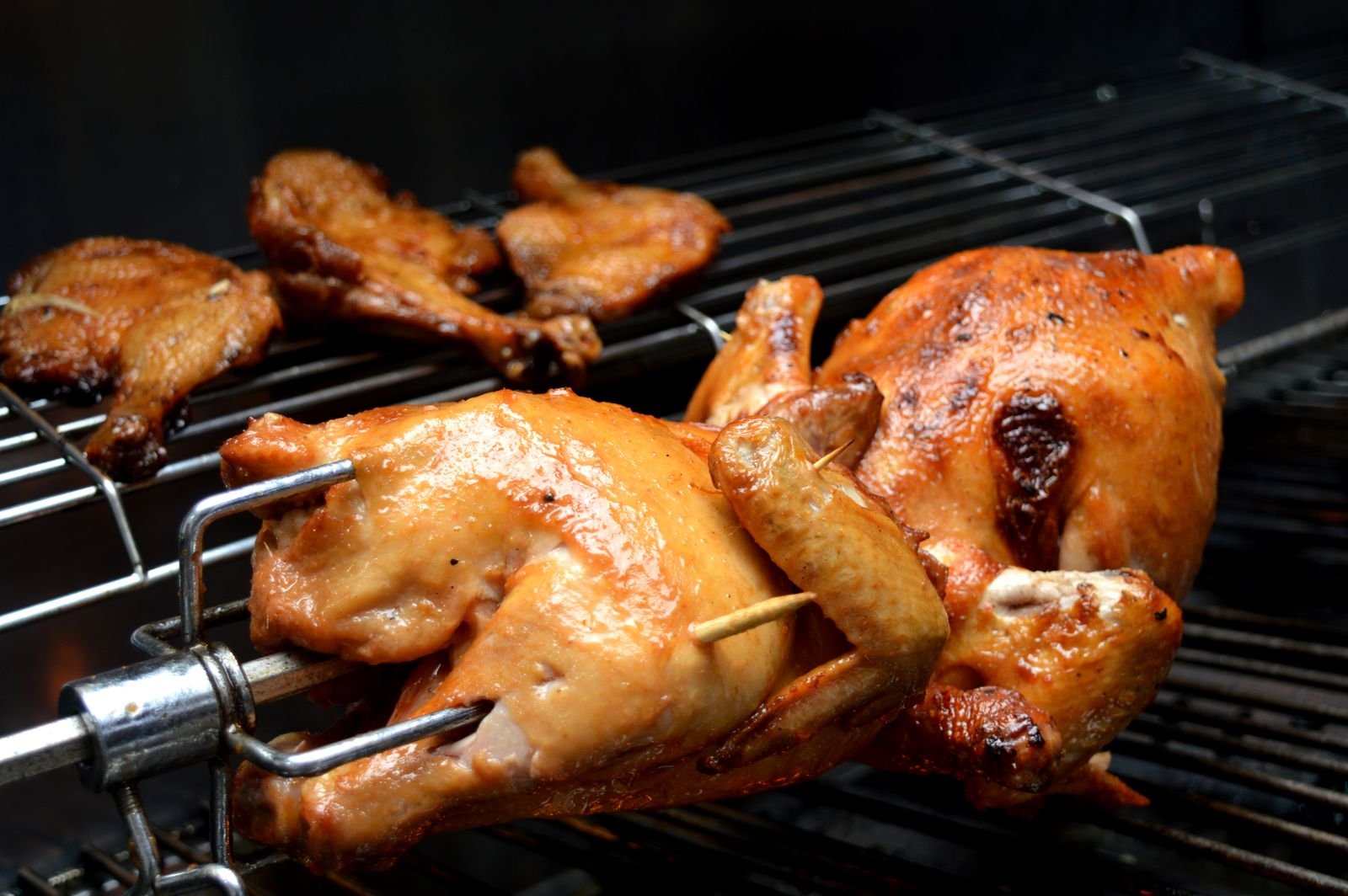 Whole chickens and chicken portions browning on a dark rotisserie grill.