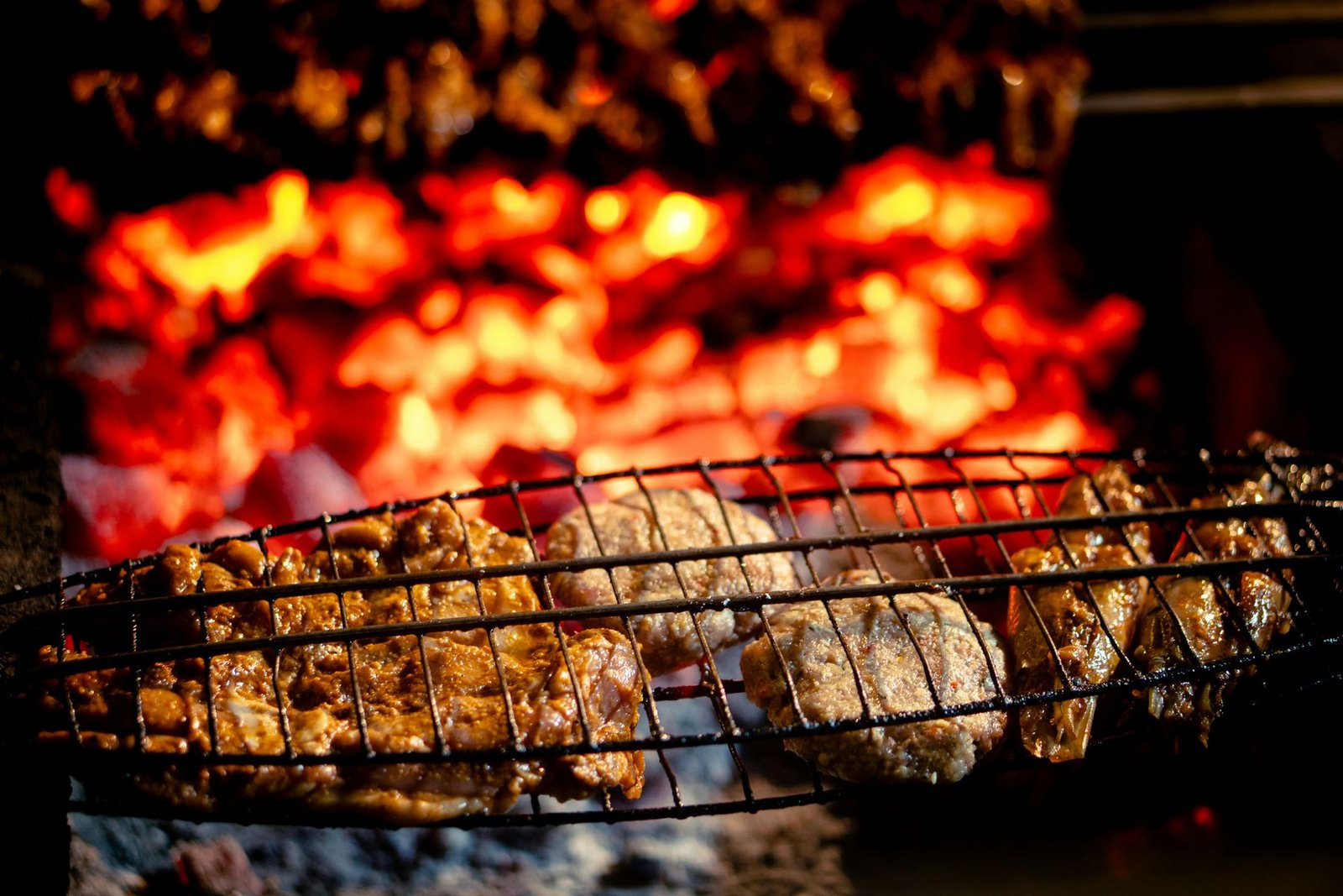 Meat cooking over glowing charcoal on a metal grill.
