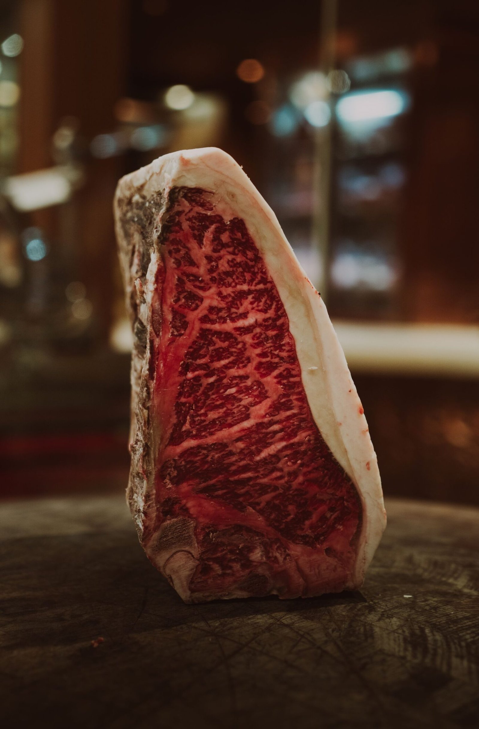 A thick raw ribeye with a heavy fat cap on a butcher block.