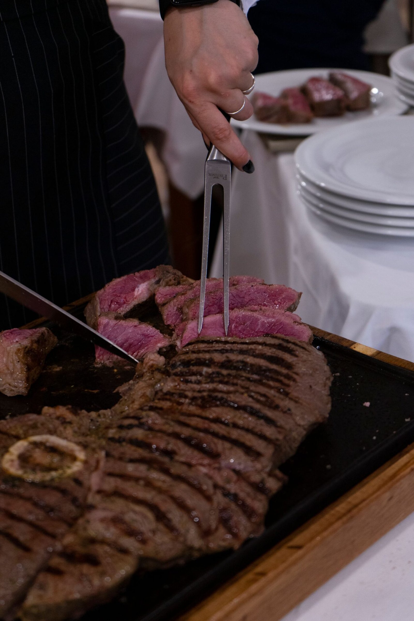 A cook carving a large medium-rare steak into thick slices.